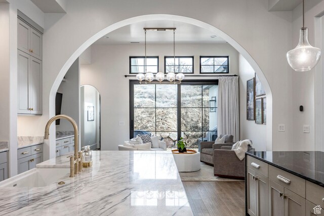 kitchen featuring light stone countertops, gray cabinetry, open floor plan, a sink, and wood finished floors