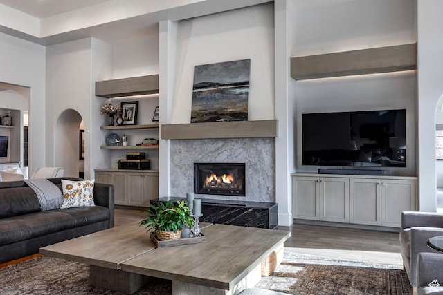 living room with arched walkways, built in shelves, a premium fireplace, and wood finished floors