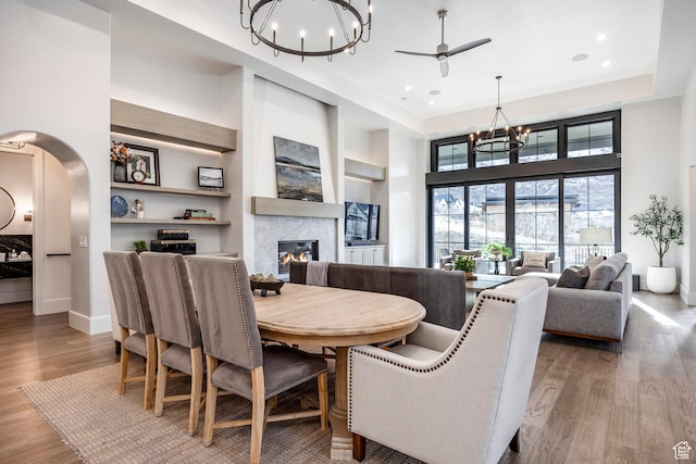 dining room featuring arched walkways, a high ceiling, a premium fireplace, wood finished floors, and baseboards