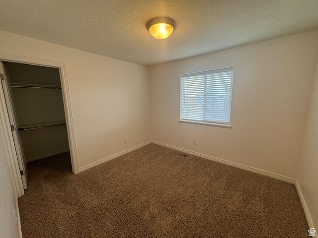unfurnished bedroom featuring a textured ceiling, baseboards, a closet, dark carpet, and a walk in closet