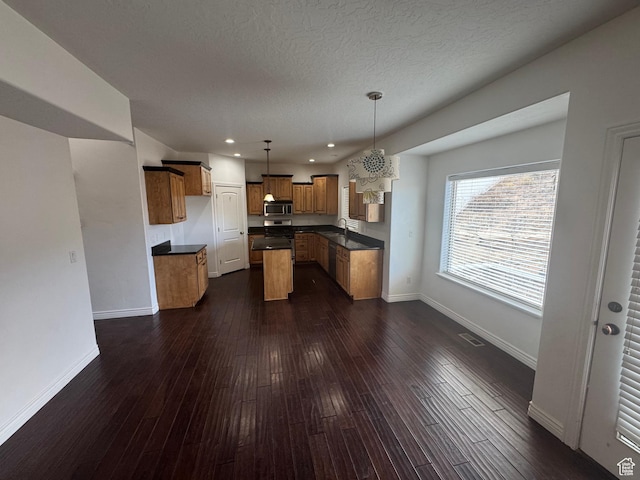 kitchen with baseboards, brown cabinetry, dark countertops, appliances with stainless steel finishes, and dark wood-type flooring