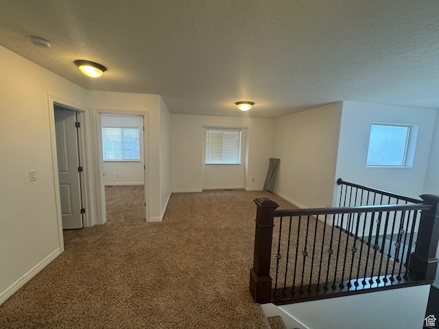 hallway featuring carpet, baseboards, a textured ceiling, and an upstairs landing