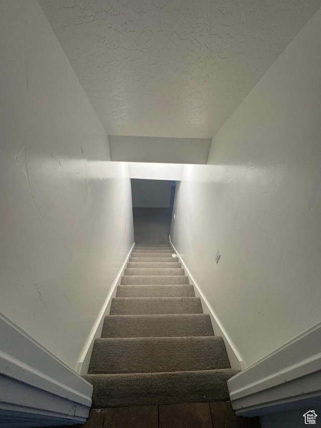 staircase featuring carpet floors, vaulted ceiling, a textured ceiling, and baseboards