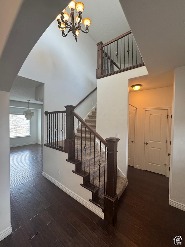 stairs with baseboards, a high ceiling, wood finished floors, and a notable chandelier