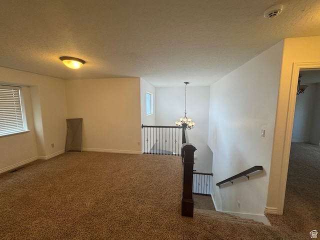 carpeted empty room with a textured ceiling, a chandelier, and baseboards