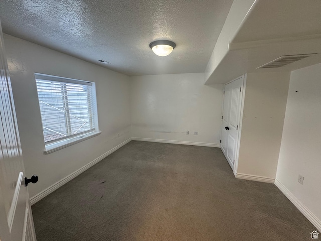 unfurnished room featuring baseboards, visible vents, dark colored carpet, and a textured ceiling