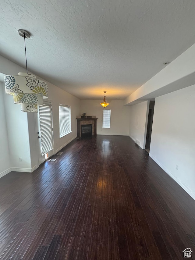 unfurnished living room featuring dark wood-style floors, visible vents, a textured ceiling, a tile fireplace, and baseboards