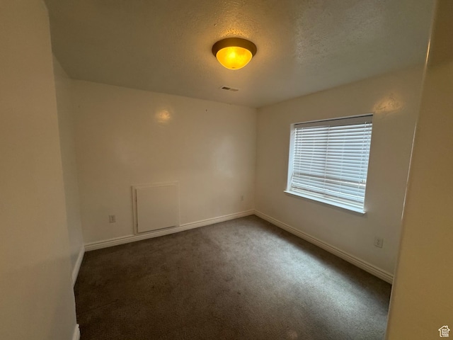 spare room featuring baseboards, visible vents, dark carpet, and a textured ceiling