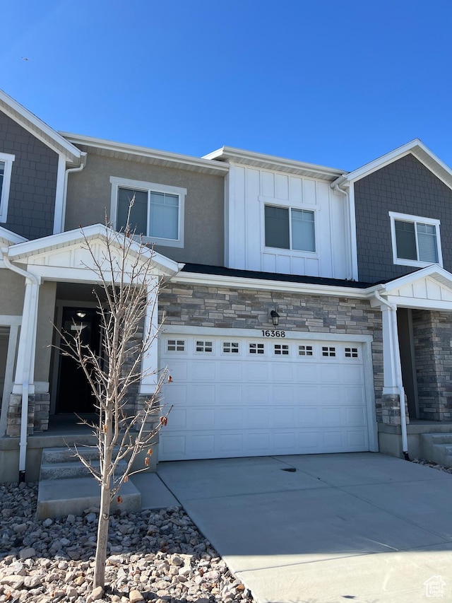 view of front of house with driveway, stone siding, an attached garage, and board and batten siding