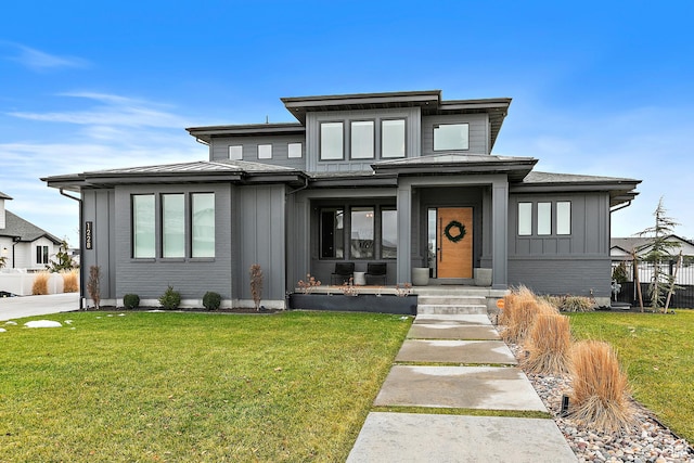 prairie-style home featuring fence, a front lawn, board and batten siding, and brick siding