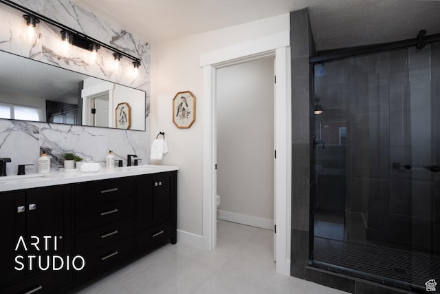 bathroom with double vanity, backsplash, toilet, a sink, and a shower stall