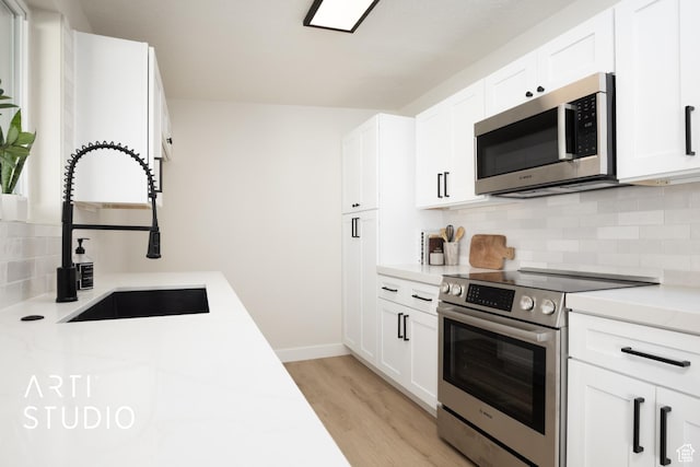 kitchen featuring a sink, stainless steel appliances, light wood-style floors, white cabinetry, and backsplash