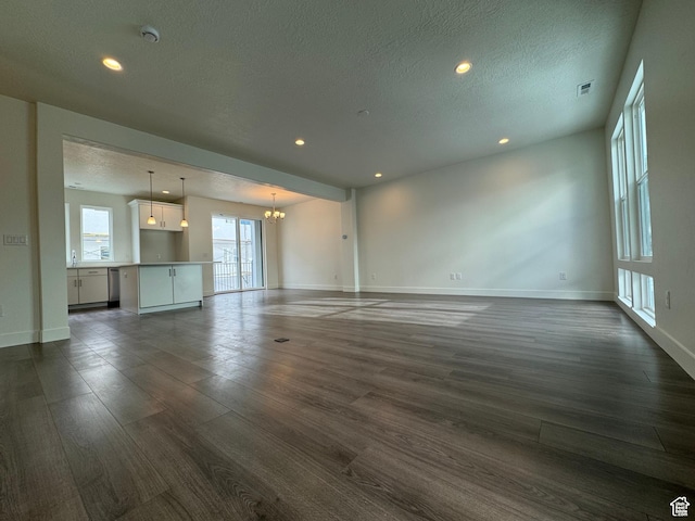 unfurnished living room featuring baseboards, dark wood finished floors, an inviting chandelier, and recessed lighting