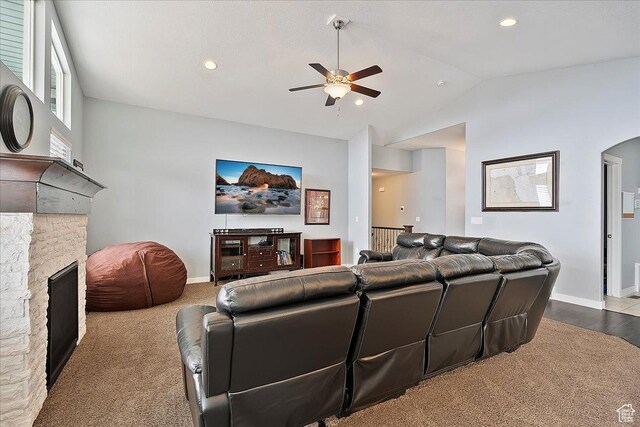 living room featuring a ceiling fan, baseboards, vaulted ceiling, and a stone fireplace