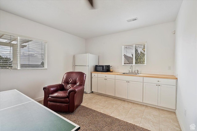 interior space featuring wooden counters, visible vents, black microwave, a sink, and freestanding refrigerator