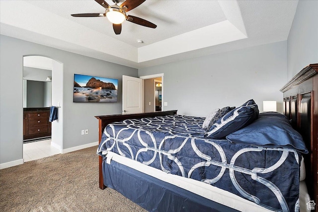 bedroom featuring carpet floors, arched walkways, a raised ceiling, and baseboards