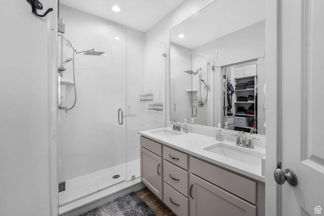 bathroom with double vanity, a shower stall, a sink, and wood finished floors