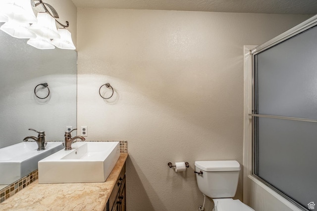 bathroom featuring toilet, a textured wall, enclosed tub / shower combo, and vanity