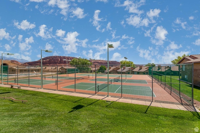 view of sport court featuring a mountain view, fence, and a lawn