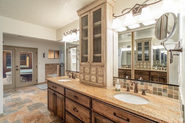 full bathroom with stone finish flooring, backsplash, and a sink