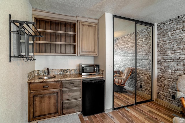 bar with light wood-style floors, stainless steel microwave, a sink, and dishwasher