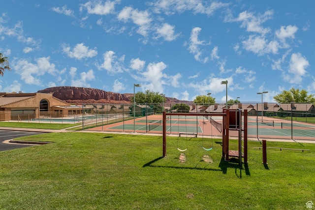 exterior space featuring a tennis court, fence, and a lawn