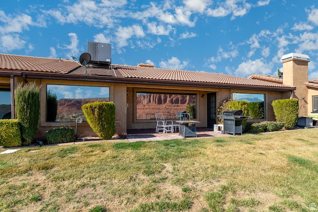 rear view of property with a tile roof, a yard, a patio area, central AC, and stucco siding