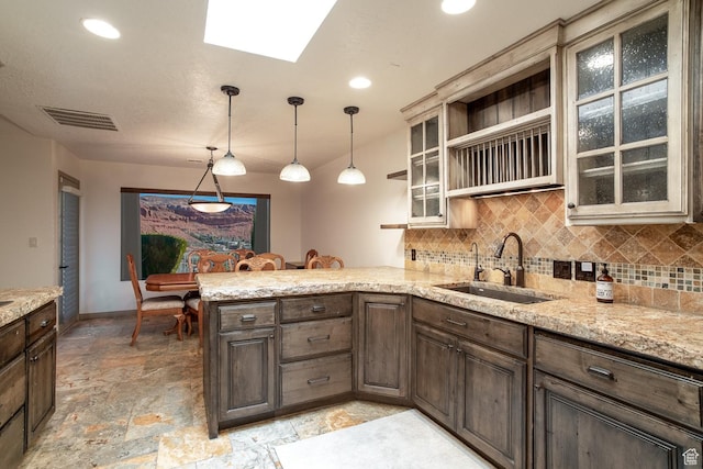 kitchen with stone tile floors, a peninsula, a sink, visible vents, and tasteful backsplash