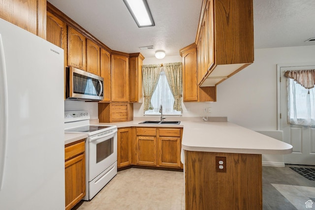 kitchen featuring a peninsula, white appliances, a wealth of natural light, and a sink