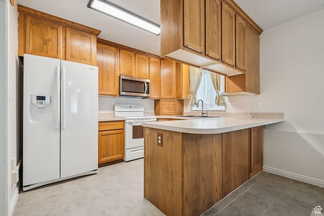 kitchen featuring light countertops, brown cabinetry, a sink, white appliances, and a peninsula
