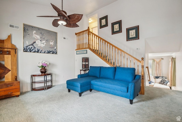 carpeted living area featuring a towering ceiling, baseboards, stairs, visible vents, and a ceiling fan