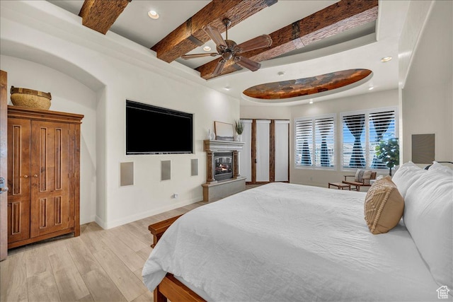 bedroom with light wood finished floors, recessed lighting, a glass covered fireplace, beamed ceiling, and baseboards