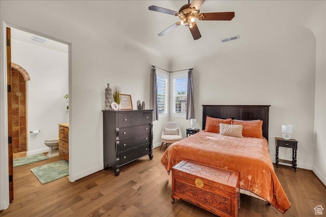 bedroom featuring arched walkways, wood finished floors, visible vents, and baseboards