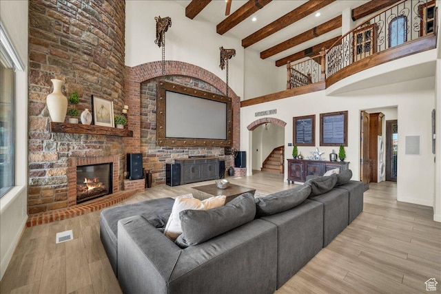 living area with a brick fireplace, beamed ceiling, stairway, and wood finished floors