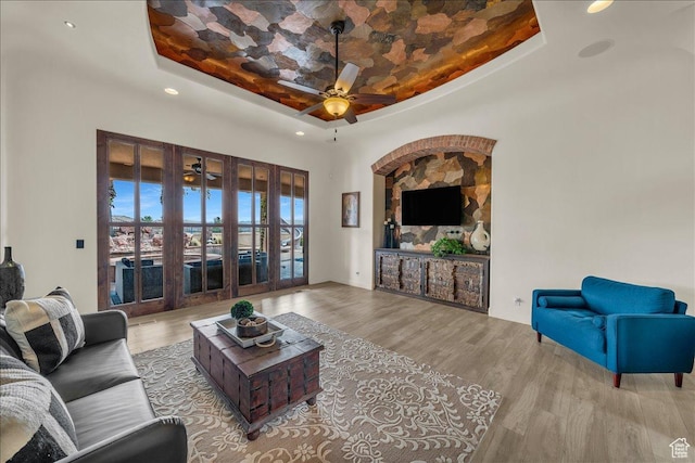 living room featuring a ceiling fan, a raised ceiling, and wood finished floors