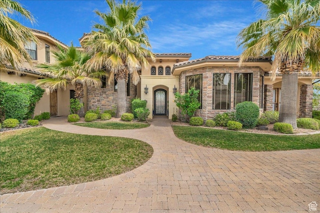 mediterranean / spanish home featuring stone siding, a front lawn, a tiled roof, and stucco siding