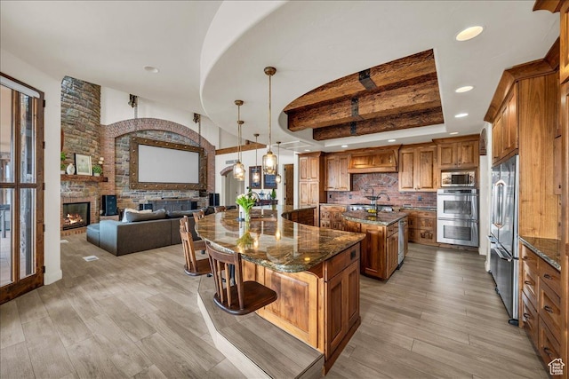 kitchen featuring a large fireplace, stainless steel appliances, a spacious island, brown cabinets, and a kitchen bar