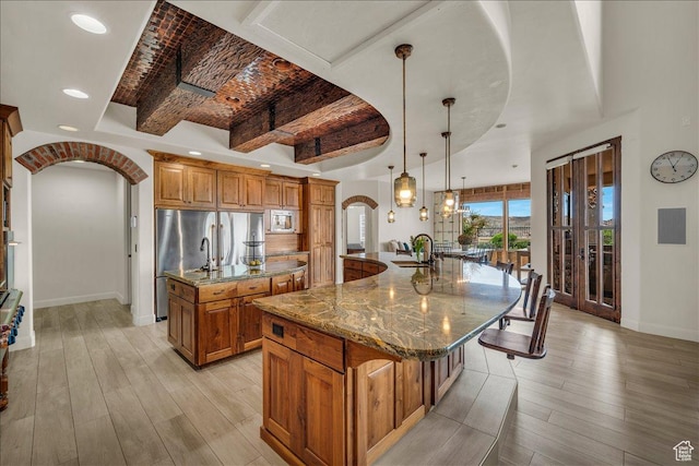 kitchen with arched walkways, a sink, brick ceiling, a large island, and brown cabinetry