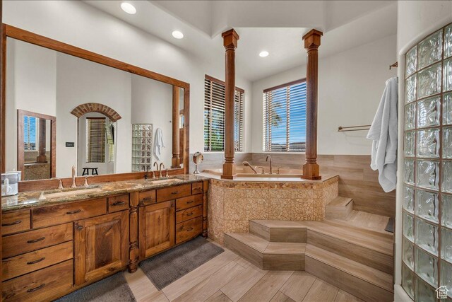 full bath with double vanity, a sink, ornate columns, and a bath