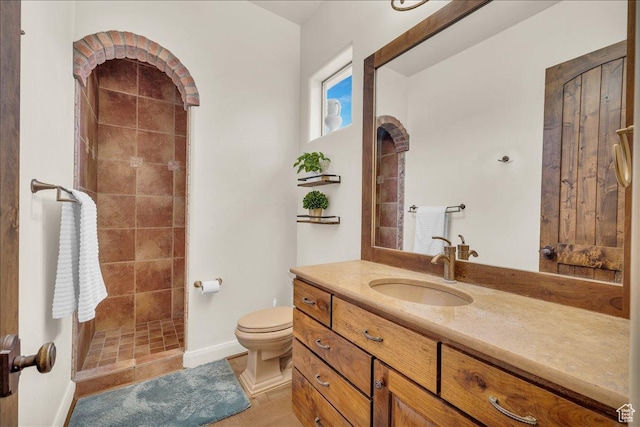 full bath with baseboards, a tile shower, vanity, and toilet