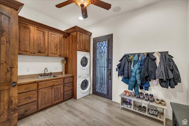 laundry area featuring stacked washer / drying machine, cabinet space, light wood-style flooring, a sink, and ceiling fan