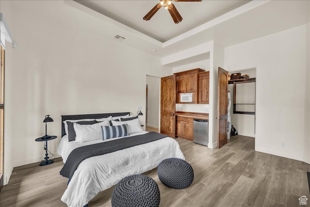 bedroom featuring visible vents, a tray ceiling, light wood-style flooring, and baseboards