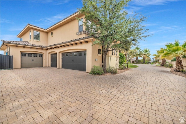 view of side of property featuring a garage, decorative driveway, a tiled roof, and stucco siding
