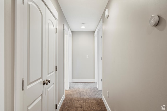 corridor featuring baseboards and dark colored carpet