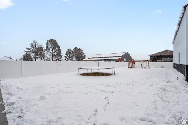 yard layered in snow featuring a trampoline and a fenced backyard