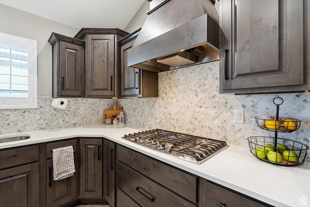 kitchen featuring stainless steel gas cooktop, dark brown cabinets, light countertops, and wall chimney range hood