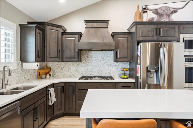 kitchen with custom range hood, a sink, appliances with stainless steel finishes, light countertops, and lofted ceiling