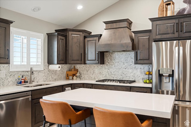 kitchen with a breakfast bar, a sink, dark brown cabinetry, appliances with stainless steel finishes, and custom exhaust hood