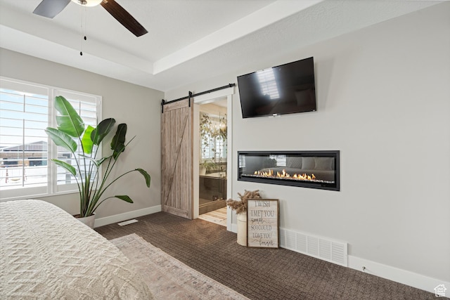 carpeted bedroom featuring visible vents, ensuite bathroom, a barn door, baseboards, and a raised ceiling