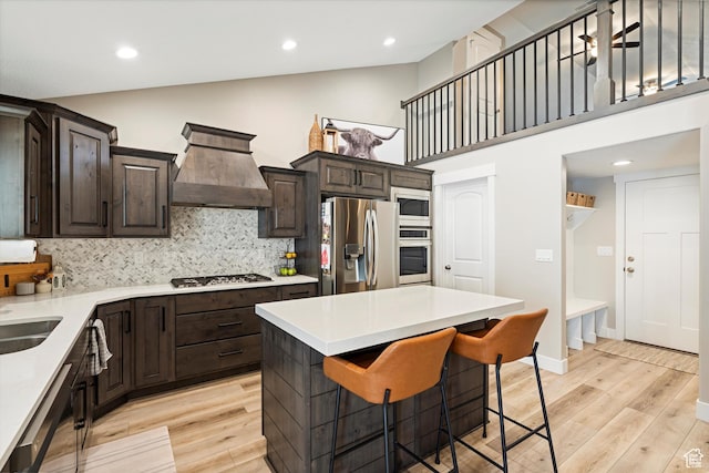 kitchen featuring premium range hood, stainless steel appliances, light wood-style floors, and dark brown cabinets